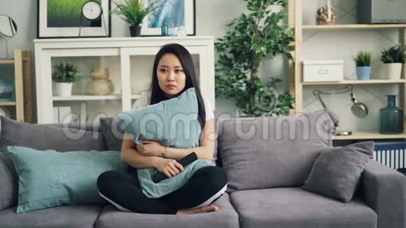美丽的亚洲年轻女子在家里拿着枕头看恐怖电影然后对恐怖事件做出反应视频的预览图