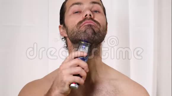英俊的年轻人留着长发在浴室里用修剪器刮胡子光线优美背景模糊视频的预览图