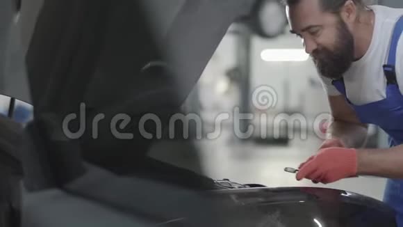 成年机械师站在汽车附近有一个开放的引擎盖并紧固螺栓与扳手在发动机关闭有胡子的人视频的预览图