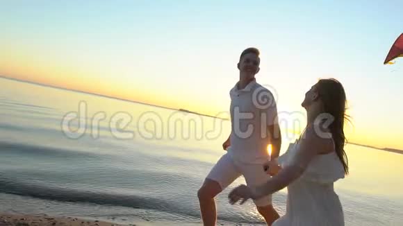 年轻的幸福夫妇在日落时在海边玩风筝男人和女人在阳光下享受时光视频的预览图