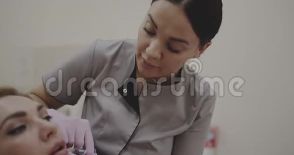 年轻的美容师为一位女士做唇部注射在电影院的Canera拍摄12位颜色深度视频的预览图