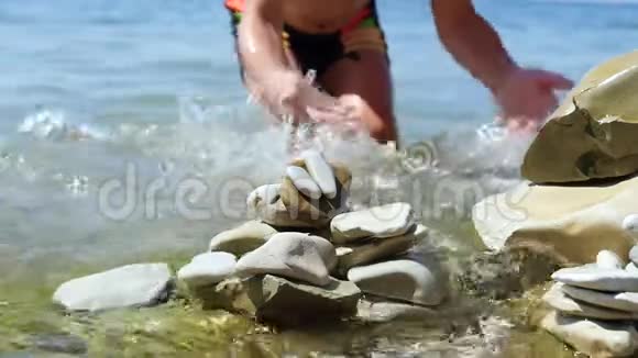 孩子和他的母亲用自己的手在沙滩上放小石子动作缓慢特写镜头视频的预览图