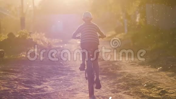 男孩骑着自行车在夕阳下沿着村庄的道路视频的预览图