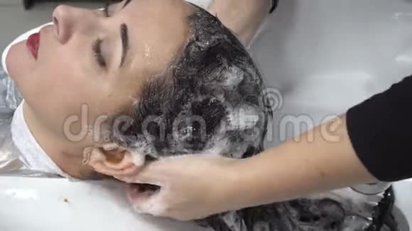特写镜头发型师用白色脸盆在一家发廊里给一位东方女性的头发梳洗头发护理4K视频的预览图