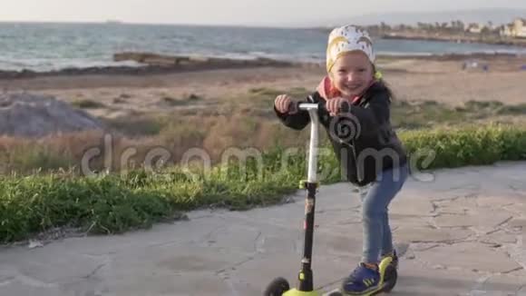 酷酷的小女孩骑着滑板车沿着大海的道路视频的预览图