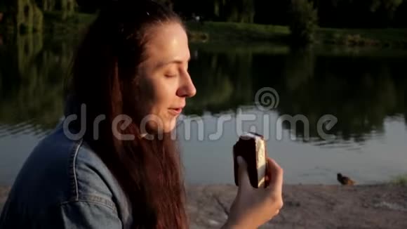 女孩躺在湖边吃着有食欲的冰淇淋享受着阳光视频的预览图