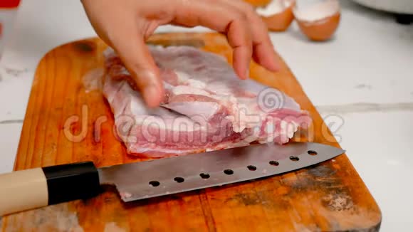 女人的手在厨房的切割板上用刀把猪肉切成碎片视频的预览图