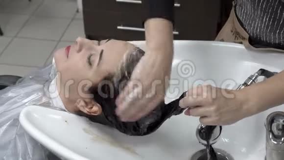 女理发师在美容院给东方女孩洗头洗发水头发护理快关门4K25fps视频的预览图