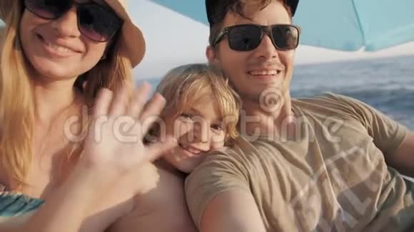 三个戴太阳镜的微笑家庭在海滩上自拍视频的预览图