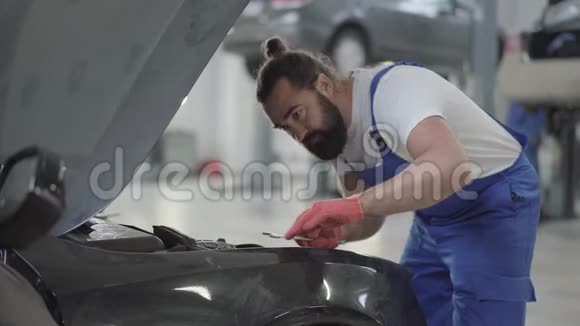 成年机械师站在汽车附近有一个开放的引擎盖并验证发动机的状况穿制服的长胡子男人视频的预览图