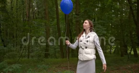 快乐的女人站着打着一个蓝色的气球在春天的树林里在斯洛文尼亚视频的预览图