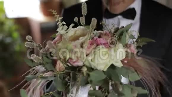 英俊的新郎站在窗边嗅着一束结婚花结婚花束商人视频的预览图