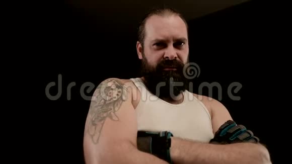 蓄胡子的男人在黑色的背景上交叉双臂做愤怒的鬼脸特写视频的预览图