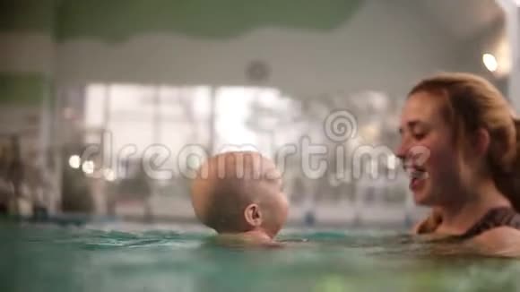 可爱的宝宝和妈妈一起上游泳课健康的母亲教孩子在游泳池游泳年轻的视频的预览图