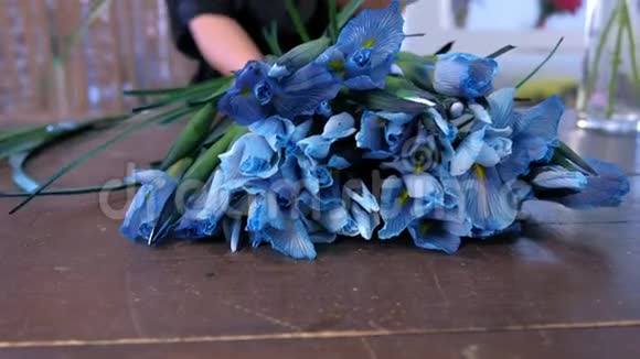 花店女店员用桌上的蓝色鸢尾花制作花束在店里出售视频的预览图