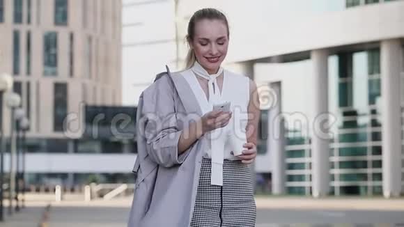 一位年轻的女商人站在市中心用智能手机端着一杯咖啡视频的预览图