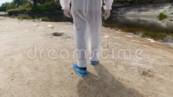 一个穿着防护服的人的腿的特写镜头他沿着一条干河散步估计污染的程度视频的预览图