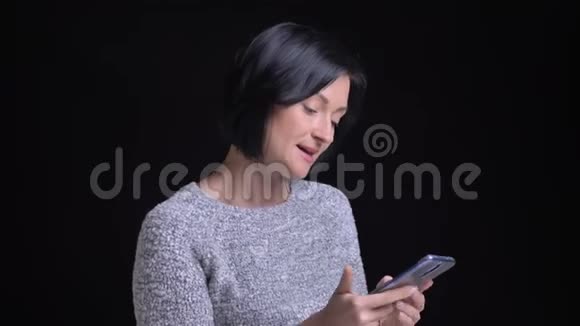 年轻美丽的白种人黑发女性的特写肖像用电话然后看着相机微笑着视频的预览图