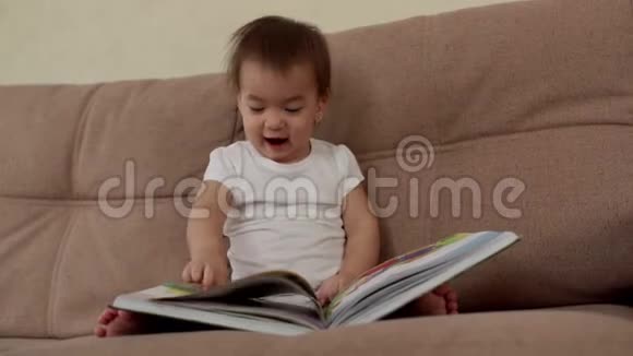 小女孩坐在柔软的沙发上笑着翻开一本五颜六色的书页视频的预览图
