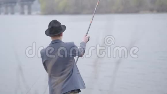 清晨年轻的渔夫穿着一件夹克和一顶带帽檐的帽子在城市附近的河里钓鱼钓竿和一个视频的预览图