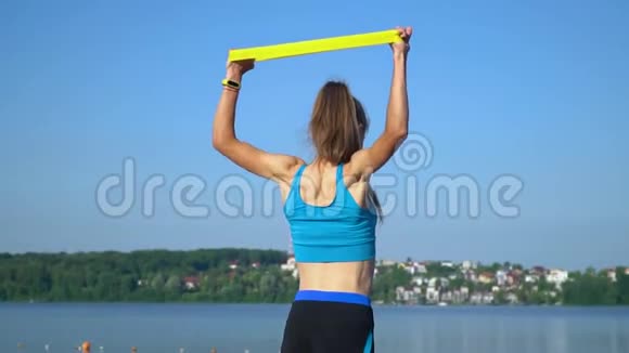 将运动型女性穿着运动服使用弹力带双手伸展全身靠近湖边视频的预览图