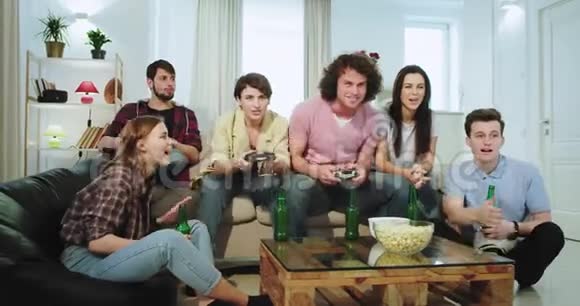 在沙发上多民族的大朋友在电视上玩电子游戏其中两个女人是赢家而家伙输了他视频的预览图