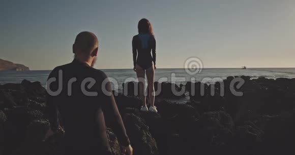在日落时分站在岩石上的湿漉漉的一对奇怪的自由夫妇用12位颜色的镜头拍摄视频的预览图