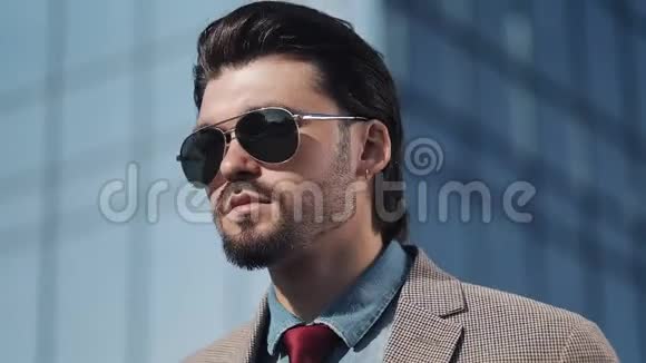 穿西装戴太阳镜的年轻英俊成功人士站在现代办公中心附近的肖像视频的预览图