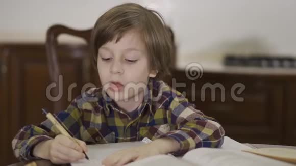 一个穿着格子衬衫坐在家里餐桌旁做作业的小男孩的肖像画小学生视频的预览图