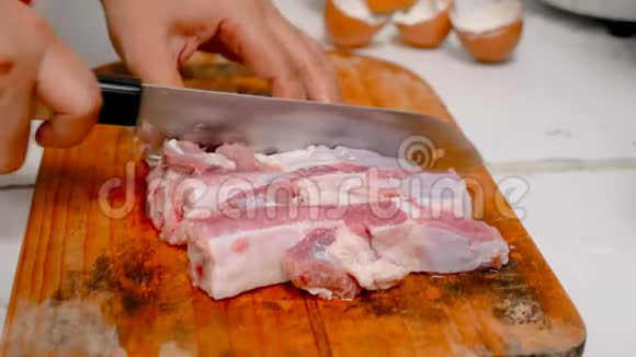 女人的手在厨房的切割板上用刀把猪肉切成碎片视频的预览图