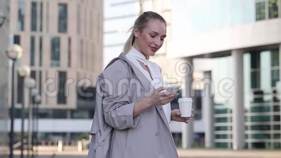 一位年轻的女商人站在市中心用智能手机端着一杯咖啡视频的预览图