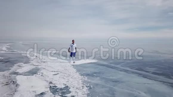 一名足球运动员站在贝加尔湖的中间美丽的贝加尔湖裂缝蓝色光泽清澈的冰腐殖质视频的预览图