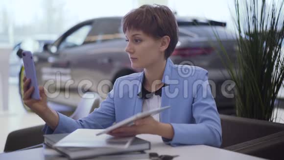 一位穿着经典蓝色正式套装留着短发的自信女人坐在桌旁用前摄像头用手机交谈视频的预览图