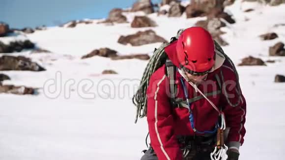 穿红色衣服的登山者带着一个带头盔和护目镜的背包他伸直绳子把绳子固定在他身上视频的预览图