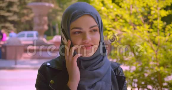 拍摄的穆斯林年轻美女戴着头巾在电话里开心地微笑着在城市的街道上聊天的特写镜头视频的预览图