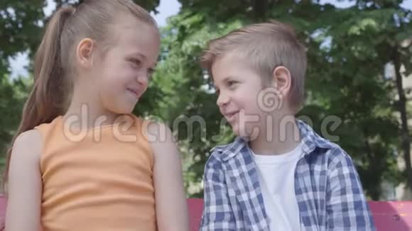 可爱的金发男孩和漂亮女孩坐在操场上秋千上的肖像几个快乐的孩子有趣的孩子视频的预览图