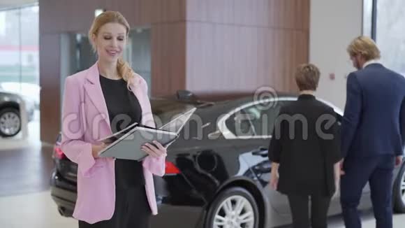 穿着粉色夹克的讨人喜欢的女人在看一本大书时的画像书上写着情侣面前的汽车信息视频的预览图
