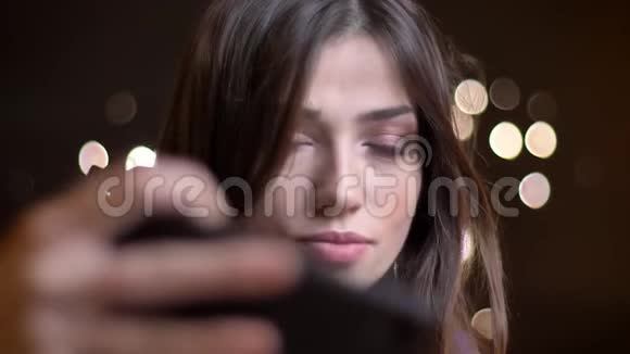 年轻漂亮的白种人女性在智能手机上自拍并用夜灯固定头发的特写照片视频的预览图