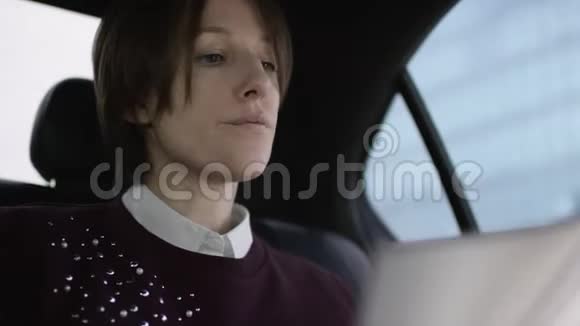 漂亮的女人棕色头发穿着白色衬衫和栗色毛衣坐在车里学习工作文件视频的预览图