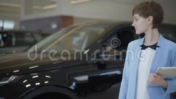 漂亮的女卖家带着平板电脑在展厅里展示了这辆车成功的女售货员站在现代视频的预览图