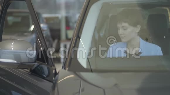 年轻漂亮的女士穿着正式的蓝色西装戴着安全带坐在汽车里的车展上现代女孩选择视频的预览图