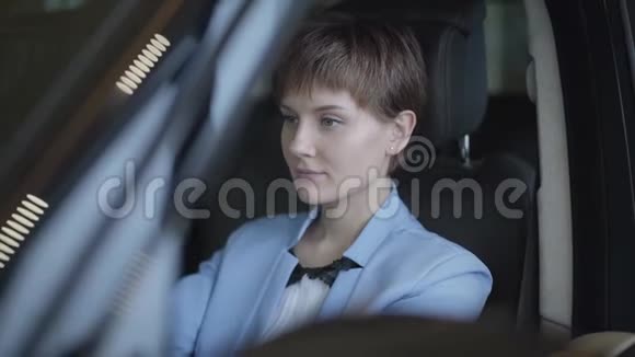 一个成功的可爱的年轻女孩的肖像她留着一头乌黑的短发穿着一套时髦的西装坐在豪华的车里电动机视频的预览图