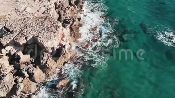 无人机拍摄了清澈透明的海浪与岩石海滩相遇悬崖飞溅创造白色泡沫奥塞亚航空景观视频的预览图