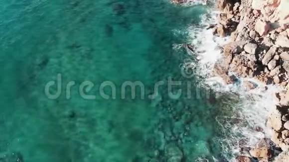 在透明蓝色清澈的海水上飞翔海浪拍打着岩石山悬崖飞溅创造了世界视频的预览图