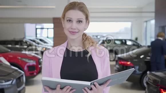 一幅穿着粉红色夹克的讨人喜欢的女人拿着一本大向镜头走去的肖像车辆在视频的预览图