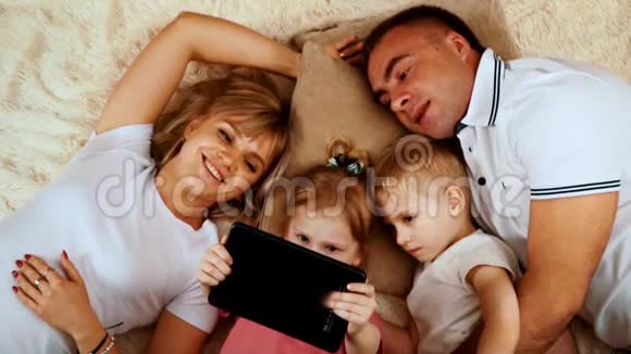 清晨白种人的一家人躺在床上看着平板电脑上的东西这让女孩保持着视频的预览图