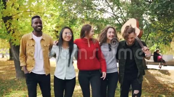 一群年轻男女的嬉皮士在公园里和吉他一起笑和说话的慢动作青年视频的预览图