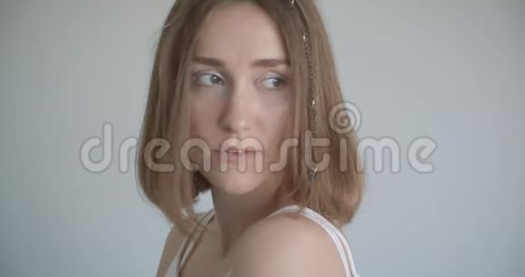 年轻漂亮的白种人女性的特写镜头她戴着发环和闪闪发光的妆容望着白色房间的一侧视频的预览图