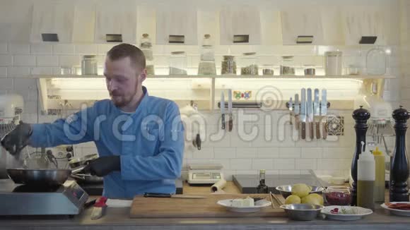 专业厨师戴黑色橡胶手套在餐厅厨房准备食物那个人拿着煎锅检查视频的预览图