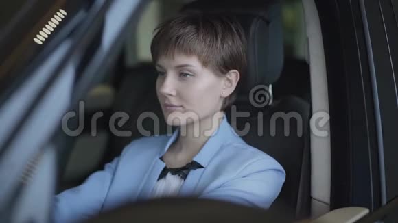 一位成功的漂亮年轻女人的肖像她留着一头乌黑的短发穿着一套时髦的西装坐在豪华的汽车上汽车视频的预览图